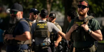 گروهی از مأموران مسلح با جلیقه‌های ضدگلوله که عبارت «POLICE HSI» روی آن‌ها درج شده است، در یک فضای باز ایستاده‌اند.