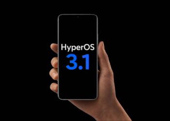 دستی که یک گوشی هوشمند را با لوگوی HyperOS 3.1 در پس‌زمینه مشکی نگه داشته است.