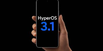 دستی که یک گوشی هوشمند را با لوگوی HyperOS 3.1 در پس‌زمینه مشکی نگه داشته است.