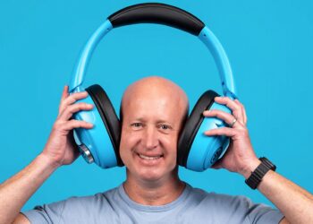 مردی که لبخند می‌زند و یک جفت هدفون آبی‌رنگ بسیار بزرگ و غیرمعمول از برند JLab را روی سر خود نگه داشته است.