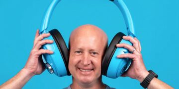 مردی که لبخند می‌زند و یک جفت هدفون آبی‌رنگ بسیار بزرگ و غیرمعمول از برند JLab را روی سر خود نگه داشته است.