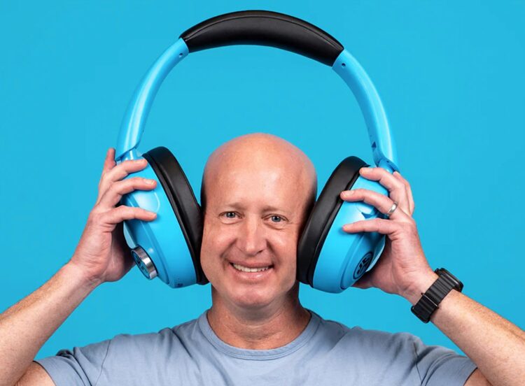 مردی که لبخند می‌زند و یک جفت هدفون آبی‌رنگ بسیار بزرگ و غیرمعمول از برند JLab را روی سر خود نگه داشته است.