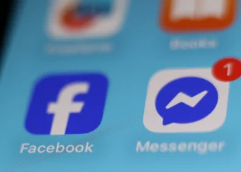 نمای نزدیک از آیکون‌های آبی رنگ فیس‌بوک و ماسنجر روی صفحه نمایش یک گوشی هوشمند.