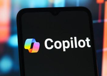 نمای نزدیک از صفحه یک گوشی هوشمند که لوگوی رنگی و متن سفید Microsoft Copilot را نمایش می‌دهد.