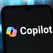 نمای نزدیک از صفحه یک گوشی هوشمند که لوگوی رنگی و متن سفید Microsoft Copilot را نمایش میدهد.
