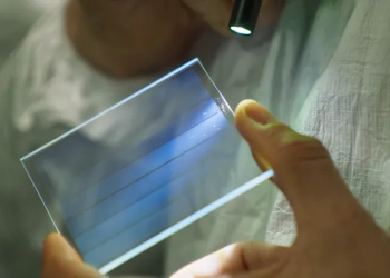 نمای نزدیک از نگه داشتن یک قطعه شیشه‌ای مربعی با خطوط آبی رنگ (Microsoft Azure) بین دو انگشت در مقابل پس‌زمینه مشکی.