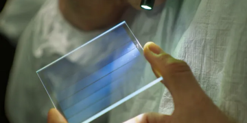 نمای نزدیک از نگه داشتن یک قطعه شیشه‌ای مربعی با خطوط آبی رنگ (Microsoft Azure) بین دو انگشت در مقابل پس‌زمینه مشکی.