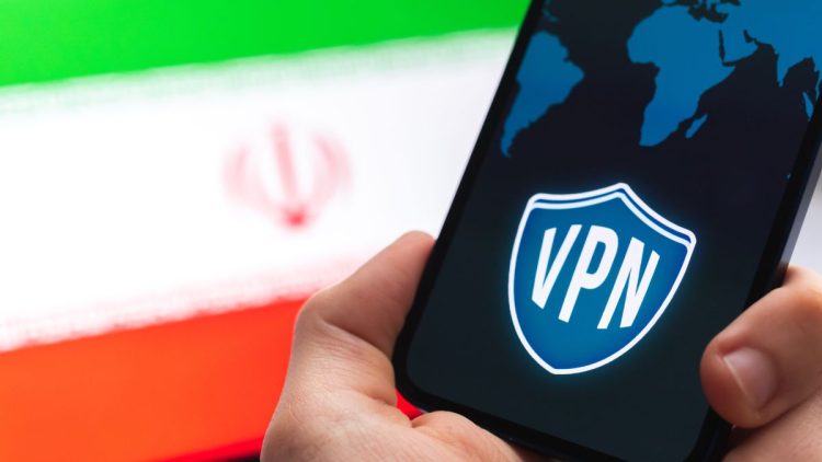 دستی که گوشی هوشمندی با نماد VPN و نقشه جهان را در مقابل پرچم ایران نگه داشته است.