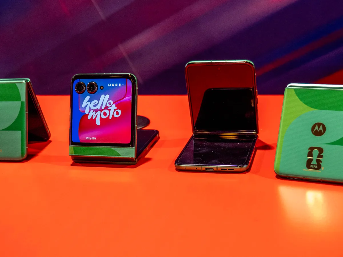 ردیفی از گوشیهای تاشو موتورولا با تم جام جهانی و والپیپر "hello moto" روی میز قرمز.