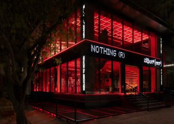 نمای بیرونی فروشگاه رسمی Nothing ® در هند، با معماری مدرن شیشه‌ای، نورپردازی قرمز چشمگیر در فضای داخلی، و لوگوی LED برند Nothing روی نمای ساختمان. طراحی مینیمال فروشگاه با ورودی پلکانی، المان‌های صنعتی و فضای شهری اطراف، هویت بصری متمایز برند را برجسته می‌کند.