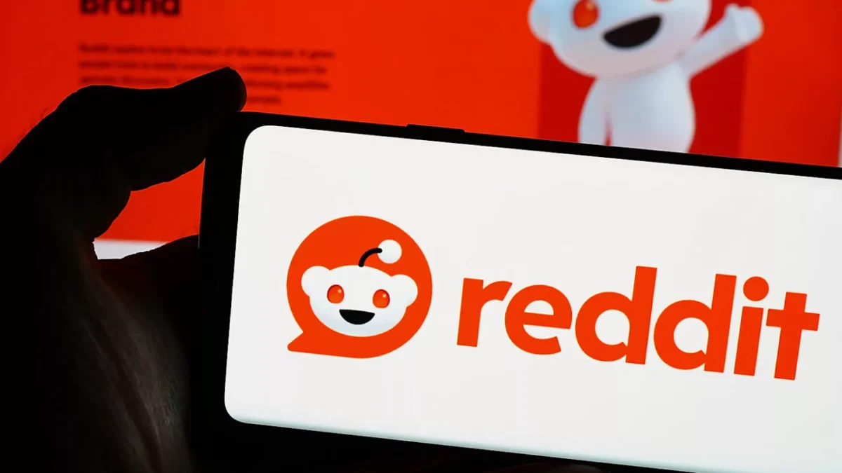 گوشی هوشمندی که لوگوی ردیت را نمایش می‌دهد و در پس‌زمینه تصویر تار از وب‌سایت ردیت دیده می‌شود.