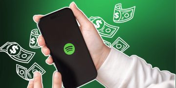 «دستی که گوشی هوشمندی با لوگوی سبز اسپاتیفای را نگه داشته و طرح‌های گرافیکی اسکناس دلار در پس‌زمینه سبز دیده می‌شود.»