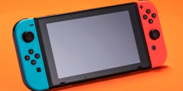 کنسول نینتندو سوییچ با جویکانهای آبی و قرمز روی پسزمینه نارنجی.
