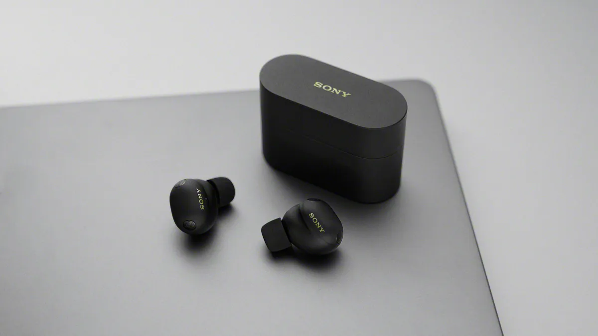 هدفون بی‌سیم Sony XM6 به رنگ مشکی در کنار کیس شارژ روی میز براق.