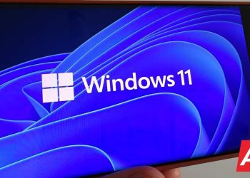 نمایش لوگوی Windows 11 و پس‌زمینه آبی انتزاعی روی صفحه‌نمایش یک گوشی هوشمند.