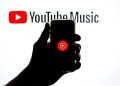 ضد نور دستی که یک گوشی هوشمند با لوگوی یوتیوب را در مقابل پس‌زمینه درخشان "YouTube Music" نگه داشته است.
