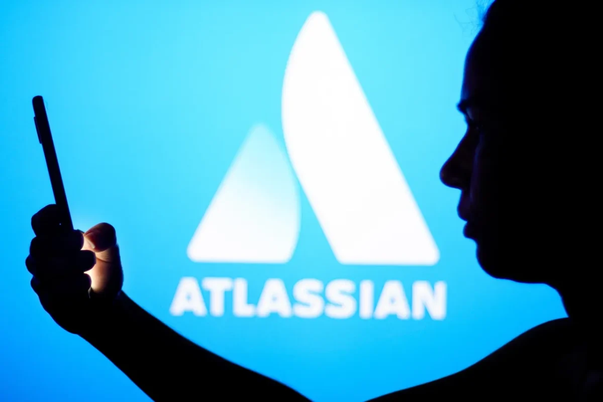 نمایی مفهومی از برند Atlassian با نمایش لوگو در پسزمینه آبی، همراه با یک دستگاه موبایل در پیشزمینه که به مشکلات یا باگهای نرمافزاری در ابزارهای سازمانی اشاره دارد