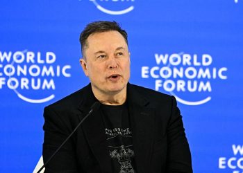 نمای یک سخنرانی رسمی در رویداد World Economic Forum با پسزمینه آبی و لوگوی تکرارشونده این رویداد جهانی. یک سخنران با پوشش رسمی در پشت تریبون و میکروفن قرار دارد و فضای تصویر، حالوهوای کنفرانس اقتصادی بینالمللی، سیاستگذاری و فناوری را منتقل میکند.