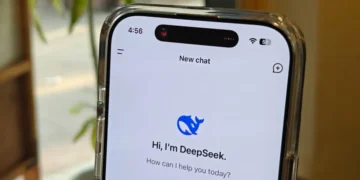 نمای نزدیک از یک گوشی هوشمند که اپلیکیشن DeepSeek AI روی صفحه آن باز است؛ متن «Hi, I’m DeepSeek. How can I help you today?» دیده می‌شود و گوشی در محیطی داخلی با نور طبیعی و گیاهان در پس‌زمینه قرار دارد.