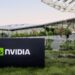 تابلوی NVIDIA در محوطه بیرونی ساختمان مدرن شرکت با معماری شیشهای و فضای سبز، نماد دفتر مرکزی و زیرساخت شرکتی انویدیا