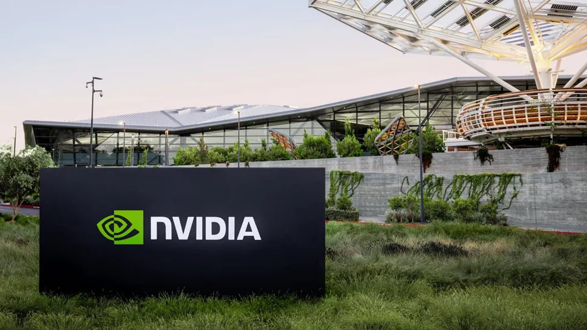 تابلوی NVIDIA در محوطه بیرونی ساختمان مدرن شرکت با معماری شیشهای و فضای سبز، نماد دفتر مرکزی و زیرساخت شرکتی انویدیا