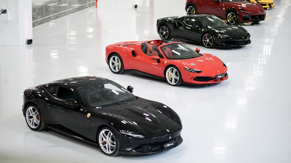 چند خودروی اسپرت Ferrari در سالن نمایش سفیدرنگ کارخانه مارانلو، شامل یک مدل قرمز روباز و چند مدل کوپه مشکی و قرمز که کنار یکدیگر پارک شده‌اند.