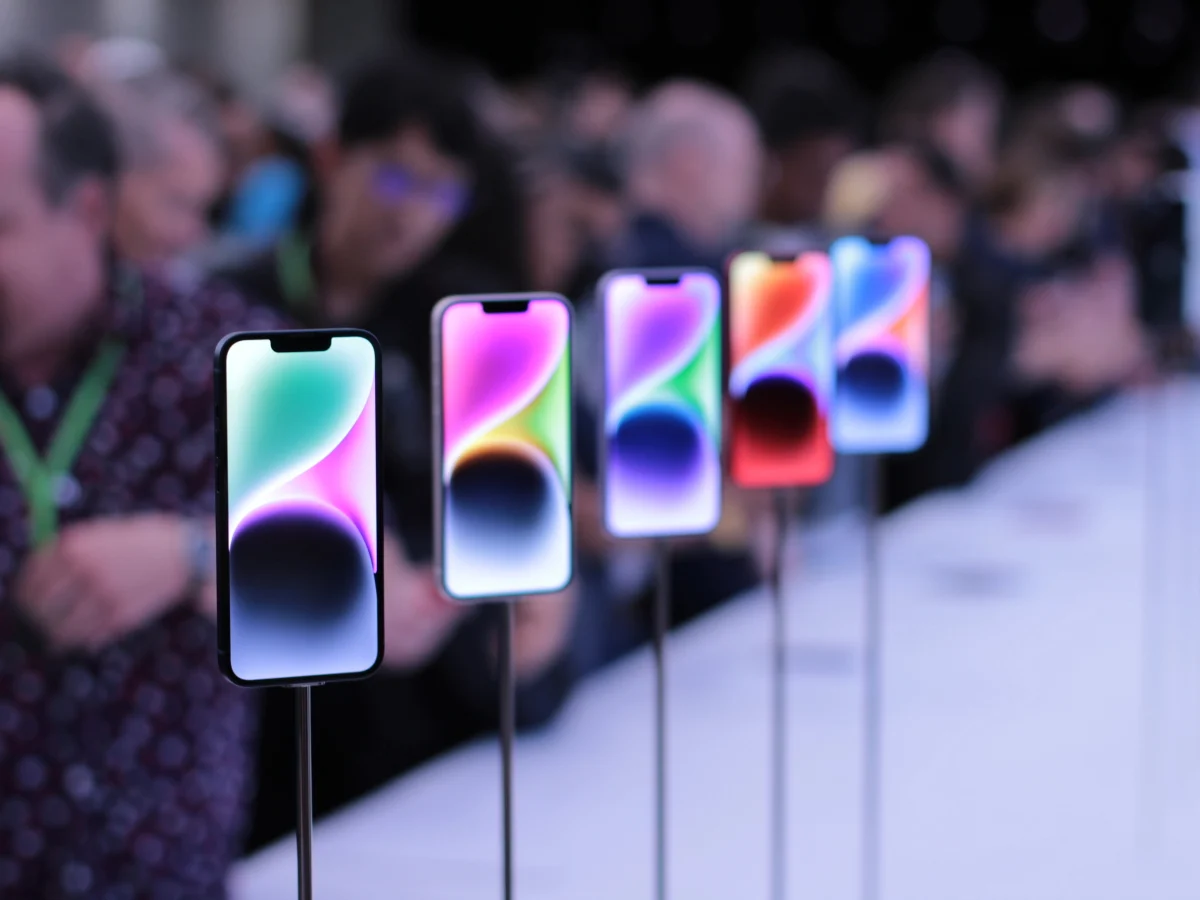 ردیفی از گوشی‌های آیفون با صفحه‌نمایش‌های رنگی که در یک رویداد عمومی روی پایه قرار گرفته‌اند.