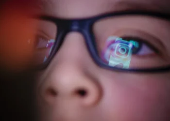 تصویر مفهومی با تمرکز بر بازتاب رابط کاربری اینستاگرام و رنگ‌های نئونی که تعامل کاربر نوجوان با شبکه اجتماعی را به صورت نمادین نشان می‌دهد