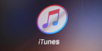 نمای نزدیک از آیکن اپلیکیشن iTunes با نماد نت موسیقی رنگی داخل یک دایره سفید، که روی صفحه‌نمایش دستگاه دیجیتال با پس‌زمینه تیره نمایش داده شده است.