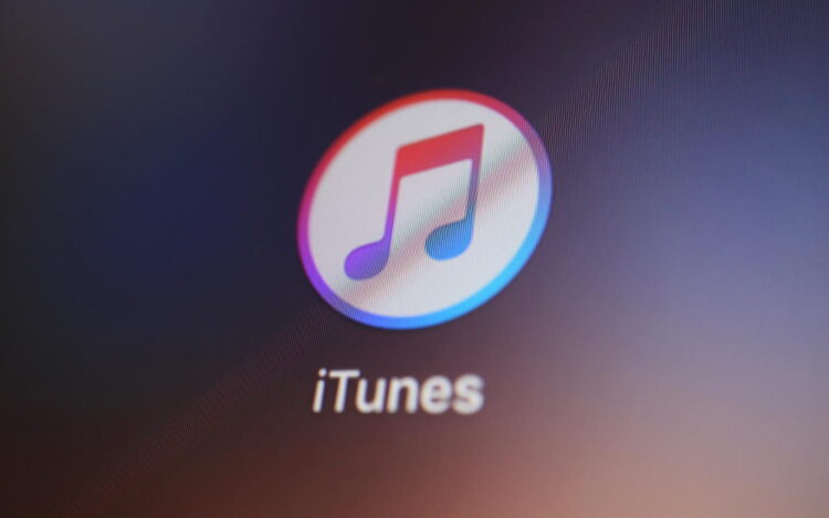 نمای نزدیک از آیکن اپلیکیشن iTunes با نماد نت موسیقی رنگی داخل یک دایره سفید، که روی صفحه‌نمایش دستگاه دیجیتال با پس‌زمینه تیره نمایش داده شده است.