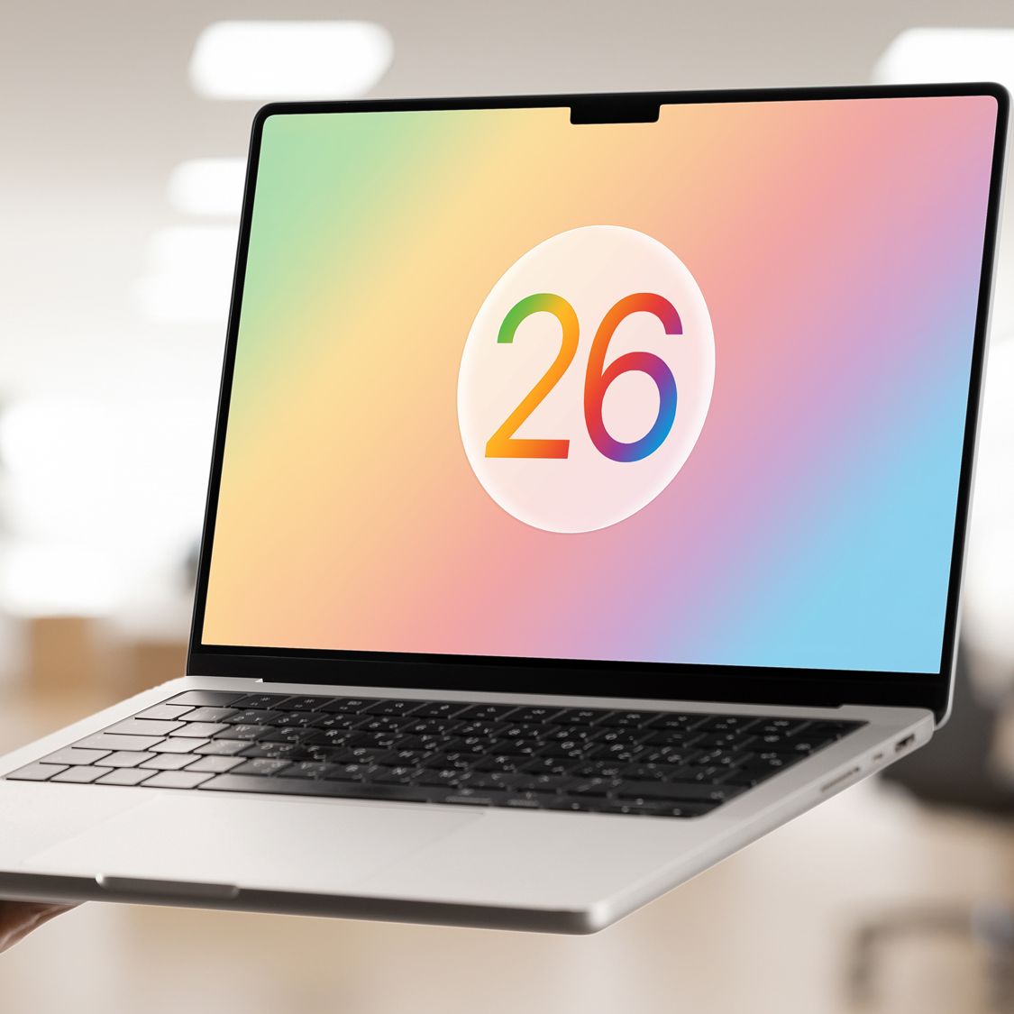 یک لپ‌تاپ مک‌بوک که عدد رنگی «26» به نشانه سیستم‌عامل macOS 26 روی صفحه نمایش آن نقش بسته است.