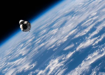 کپسول فضایی Crew Dragon متعلق به SpaceX در مدار پایین زمین، با نمای خمیده زمین، ابرها و لایه اتمسفر در پس‌زمینه؛ تصویری مرتبط با بازگشت مأموریت Crew‑2 ناسا.