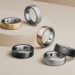نمای استودیویی از چند مدل Oura Ring 4 در رنگ‌های مشکی، نقره‌ای، طلایی و برنزی روی سطح پله‌ای؛ تمرکز بر طراحی لوکس، سنسورهای داخلی و کاربرد حلقه هوشمند در پایش خواب و سلامت