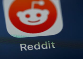 نمای نزدیک از آیکون اپلیکیشن Reddit روی صفحه نمایش گوشی هوشمند با پس‌زمینه تیره