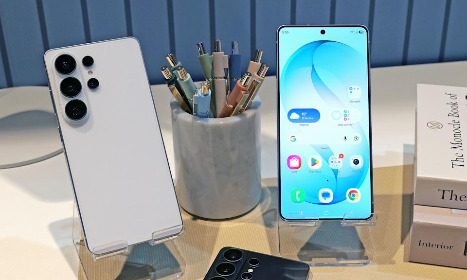 گوشی گلکسی S26 Ultra به رنگ سفید در کنار صفحه روشن آن که والپیپر آبی و آیکونهای اپلیکیشن را نشان میدهد.