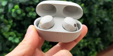 نمای نزدیک از هدفون‌های بی‌سیم سونی مدل WF-1000XM5 داخل کیس شارژ که توسط دست نگه داشته شده است.