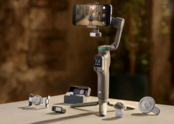 گیمبال موبایل DJI Osmo با گوشی متصل در حال ضبط ویدیو، به‌همراه لوازم جانبی مانند میکروفون، پایه نگهدارنده و ریموت کنترل روی میز