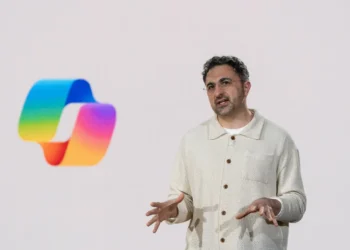 تصویر ارائه‌ای با پس‌زمینه سفید که در آن لوگوی رنگین‌کمانی Microsoft Copilot در سمت چپ دیده می‌شود و فردی در سمت راست در حال توضیح دادن با حرکات دست است؛ نمایی مفهومی از معرفی قابلیت‌های هوش مصنوعی کوپایلت مایکروسافت