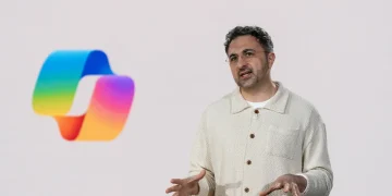 تصویر ارائه‌ای با پس‌زمینه سفید که در آن لوگوی رنگین‌کمانی Microsoft Copilot در سمت چپ دیده می‌شود و فردی در سمت راست در حال توضیح دادن با حرکات دست است؛ نمایی مفهومی از معرفی قابلیت‌های هوش مصنوعی کوپایلت مایکروسافت