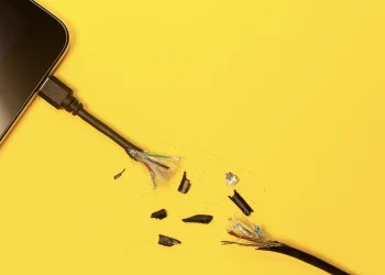 کابل شارژر گوشی پاره و فرسوده با سیم‌های داخلی نمایان روی پس‌زمینه زرد، نمادی از آسیب‌دیدگی تجهیزات و کاهش کارایی باتری