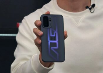 نمای نزدیک از فردی که یک گوشی OnePlus با طراحی گرافیکی بنفش درخشان روی قاب پشتی و ماژول دوربین دوگانه در گوشه چپ بالا را در دست گرفته است؛ دستگاه با نور LED الگوی خطی روی قاب روشن شده است