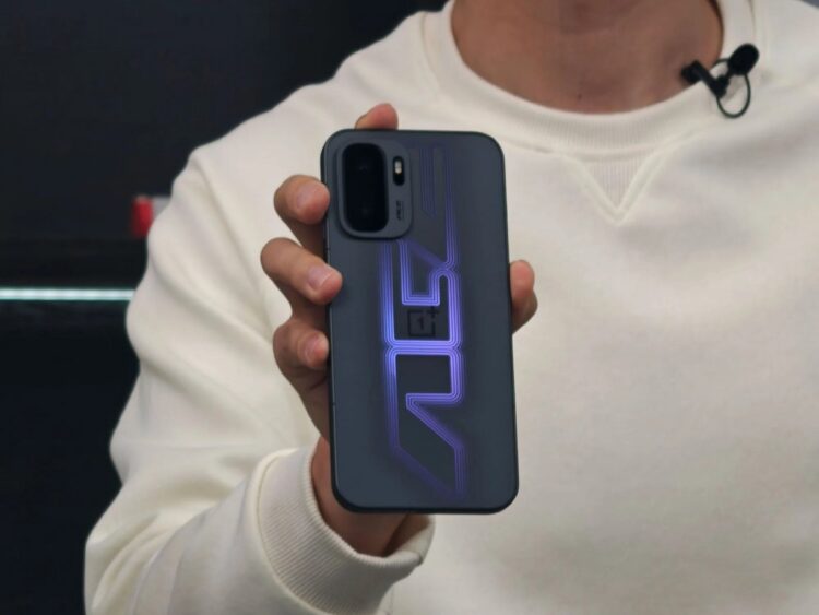 نمای نزدیک از فردی که یک گوشی OnePlus با طراحی گرافیکی بنفش درخشان روی قاب پشتی و ماژول دوربین دوگانه در گوشه چپ بالا را در دست گرفته است؛ دستگاه با نور LED الگوی خطی روی قاب روشن شده است