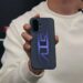 نمای نزدیک از فردی که یک گوشی OnePlus با طراحی گرافیکی بنفش درخشان روی قاب پشتی و ماژول دوربین دوگانه در گوشه چپ بالا را در دست گرفته است؛ دستگاه با نور LED الگوی خطی روی قاب روشن شده است