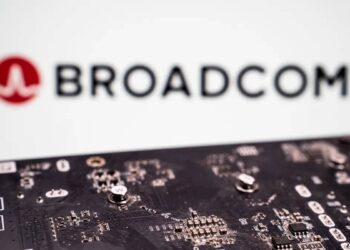برد مدار چاپی با قطعات الکترونیکی در نمای نزدیک که در جلوی تصویر قرار دارد و لوگو و نام Broadcom به‌صورت محو در پس‌زمینه دیده می‌شود؛ تصویری مرتبط با فناوری شبکه، چیپ‌ست‌ها و صنعت نیمه‌رسانا