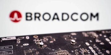 برد مدار چاپی با قطعات الکترونیکی در نمای نزدیک که در جلوی تصویر قرار دارد و لوگو و نام Broadcom به‌صورت محو در پس‌زمینه دیده می‌شود؛ تصویری مرتبط با فناوری شبکه، چیپ‌ست‌ها و صنعت نیمه‌رسانا