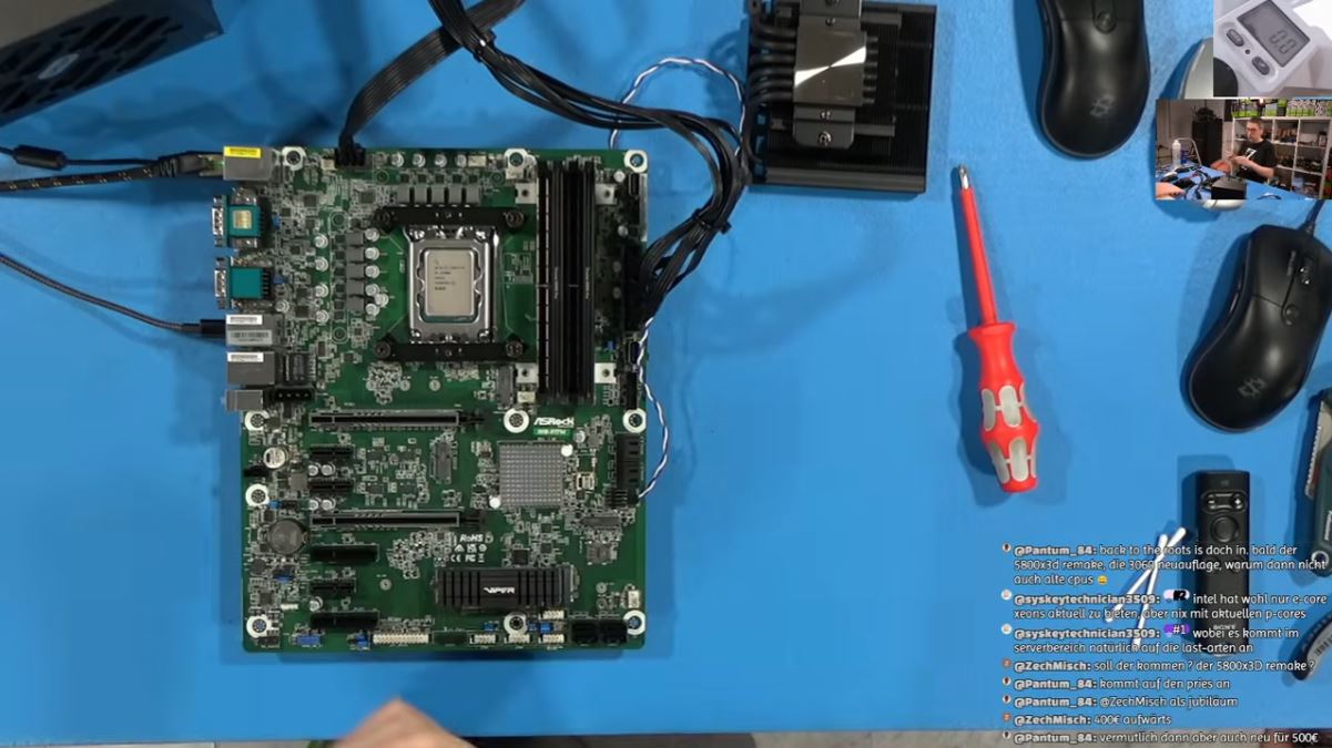 مادربرد ASRock با پردازنده نصب‌شده روی سوکت، کابل‌های پاور، خنک‌کننده CPU و ابزارهای تست روی میز آبی در یک محیط اسمبل و عیب‌یابی سیستم