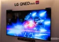 تلویزیون بزرگ LG QNED evo AI روی دیوار نمایشگاهی که صحنهای علمیتخیلی با نورهای آبی و قرمز را نمایش میدهد؛ واترمارک Android Authority در گوشه تصویر دیده میشود