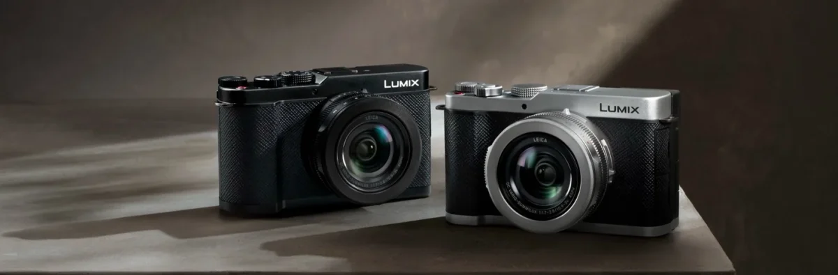 دو دوربین Lumix با بدنه نقره‌ای و مشکی کنار هم روی سطح روشن در نور استودیویی.