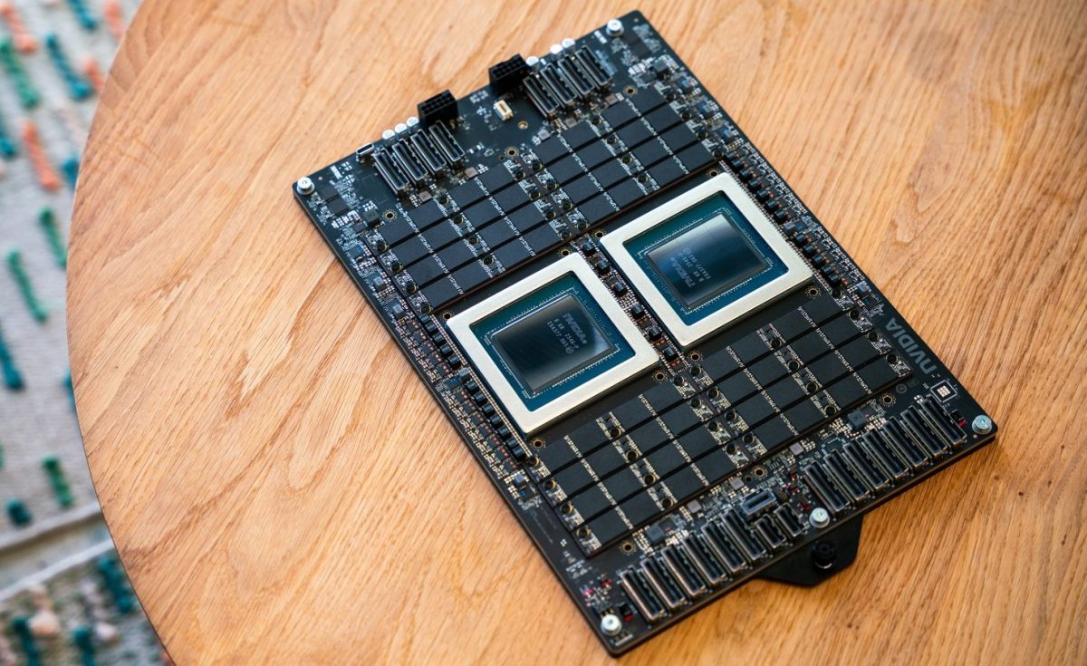 نمای نزدیک از برد مدار چاپی (PCB) قدرتمند انویدیا با دو پردازنده مرکزی (CPU) بزرگ و متمرکز، احاطه شده توسط آرایههای متعددی از تراشههای حافظه، که روی یک سطح چوبی قرار گرفته است.