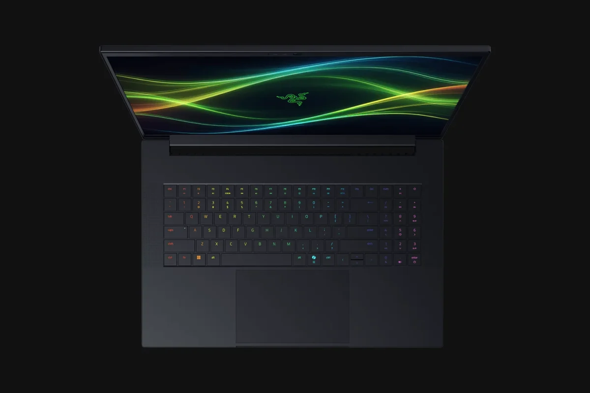 تصویر یک لپ‌تاپ Razer Blade از زاویه مستقیم بالا را نشان می‌دهد. صفحه‌نمایش نیمه‌باز است و یک پس‌زمینه با خطوط موجی سبز، زرد و آبی نمایش داده می‌شود. کیبورد دارای نورپردازی RGB است و روی پس‌زمینه مشکی قرار دارد.